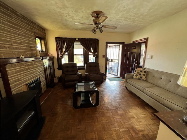 living room featuring dark parquet flooring, a textured ceiling, a stone fireplace, and ceiling fan