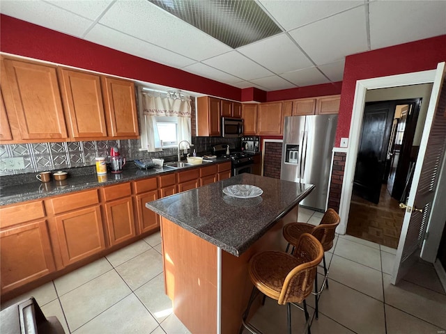 kitchen featuring a drop ceiling, stainless steel appliances, a kitchen bar, decorative backsplash, and a kitchen island