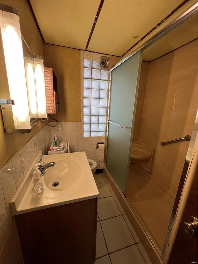 bathroom featuring tile patterned flooring, toilet, a shower with door, vanity, and tile walls