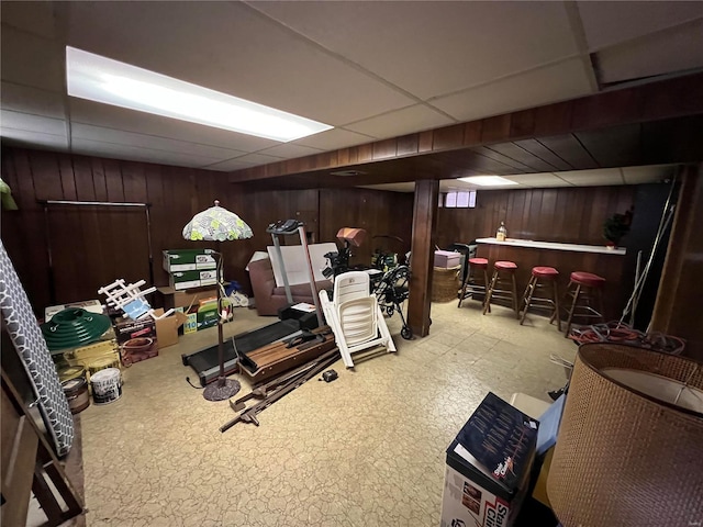 basement featuring a drop ceiling, wood walls, and bar