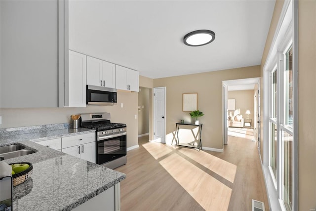 kitchen featuring light hardwood / wood-style floors, light stone counters, white cabinetry, and appliances with stainless steel finishes