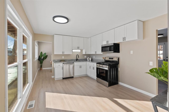 kitchen featuring white cabinetry, sink, light stone counters, light hardwood / wood-style flooring, and appliances with stainless steel finishes