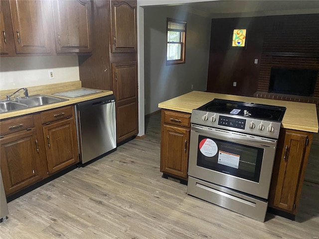 kitchen with a fireplace, sink, stainless steel appliances, and light hardwood / wood-style flooring