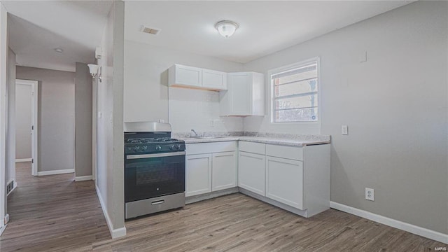 kitchen with light wood-type flooring, stainless steel gas stove, white cabinets, and sink