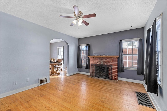 unfurnished living room featuring light hardwood / wood-style floors, a textured ceiling, a brick fireplace, and ceiling fan