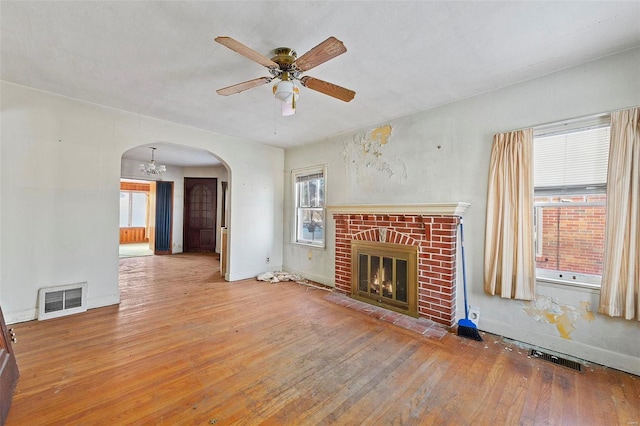 unfurnished living room with a brick fireplace, hardwood / wood-style floors, a wealth of natural light, and ceiling fan with notable chandelier