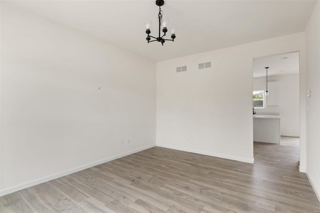 spare room with a notable chandelier and light hardwood / wood-style flooring