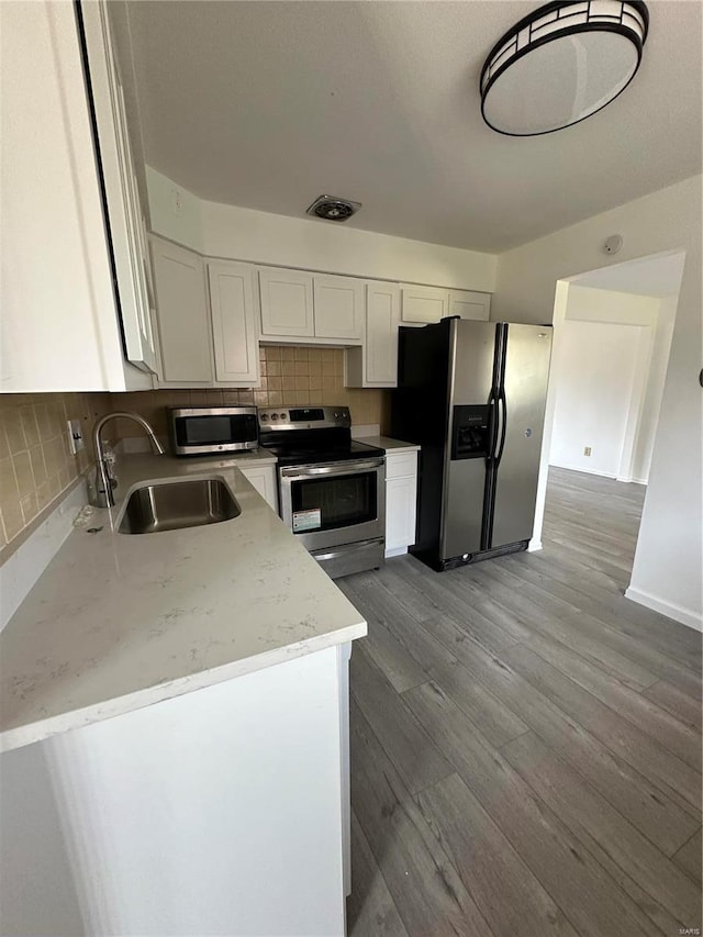 kitchen featuring light stone countertops, white cabinetry, sink, stainless steel appliances, and tasteful backsplash