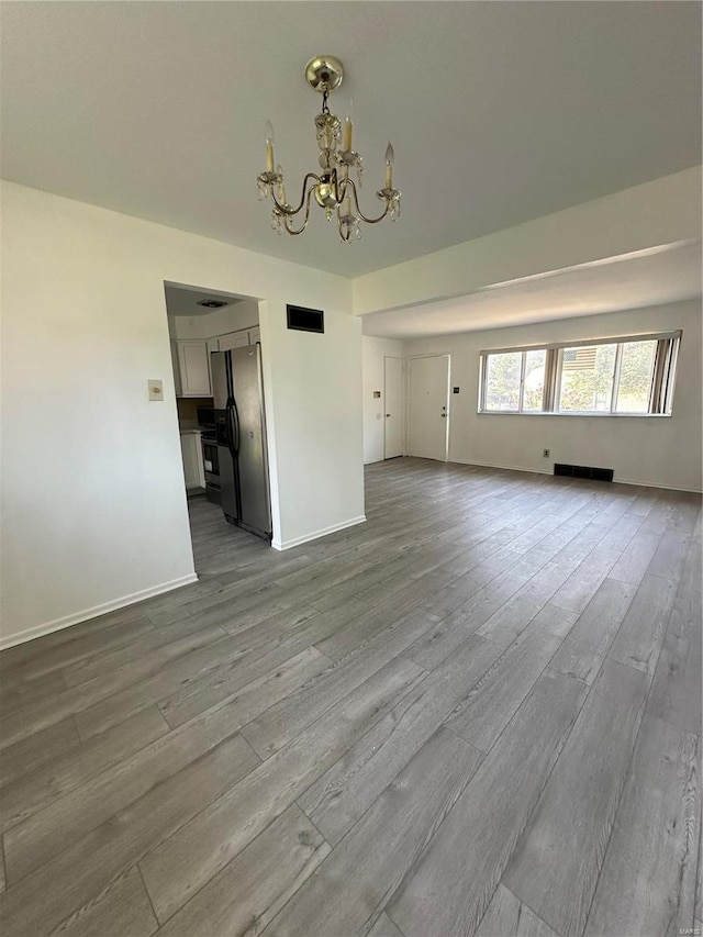 unfurnished living room featuring light wood-type flooring and a notable chandelier