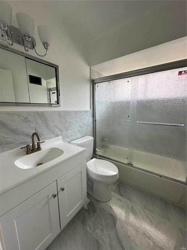 full bathroom with vanity, toilet, tile walls, and bath / shower combo with glass door