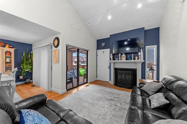 living room with baseboards, high vaulted ceiling, wood finished floors, and a fireplace