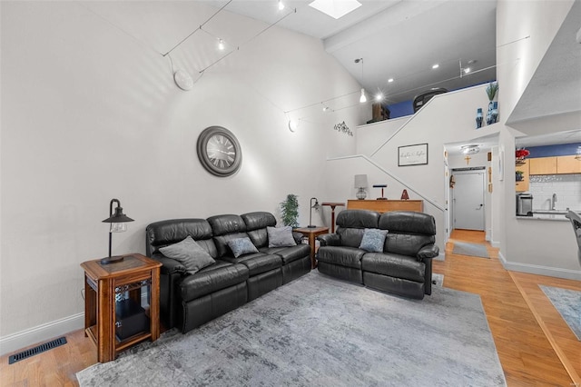 living area with light wood-type flooring, baseboards, visible vents, and high vaulted ceiling