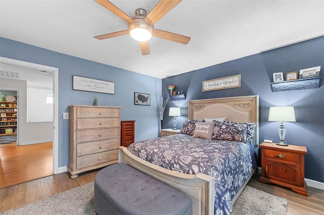 bedroom with ceiling fan, visible vents, baseboards, and wood finished floors