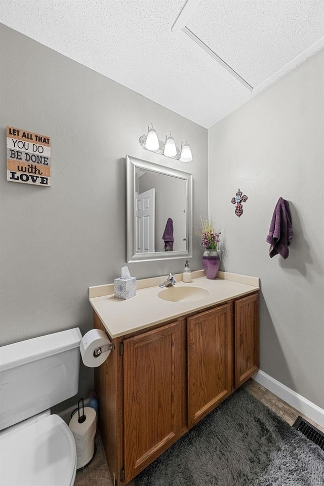 half bath with visible vents, toilet, a textured ceiling, baseboards, and vanity