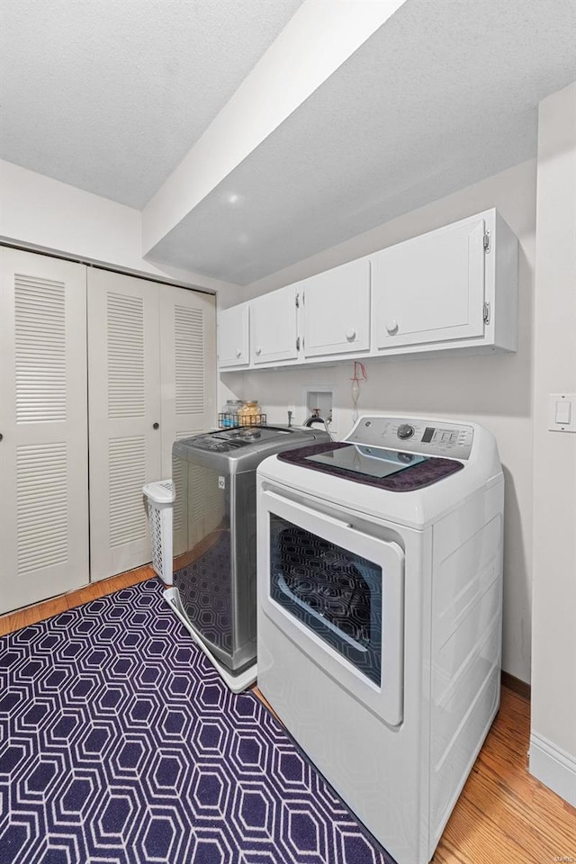 clothes washing area featuring washing machine and clothes dryer, baseboards, light wood-style floors, cabinet space, and a textured ceiling