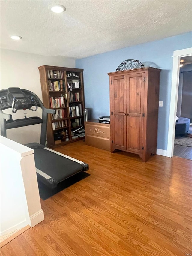 exercise area featuring light wood-style flooring, a textured ceiling, and baseboards