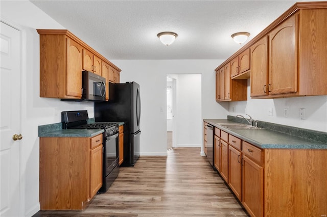 kitchen with black gas range, dishwasher, sink, light wood-type flooring, and a textured ceiling