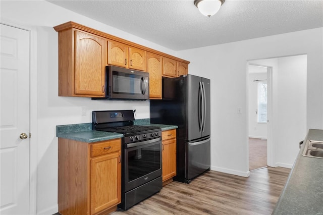 kitchen featuring black range with gas stovetop, sink, a textured ceiling, wood-type flooring, and stainless steel refrigerator