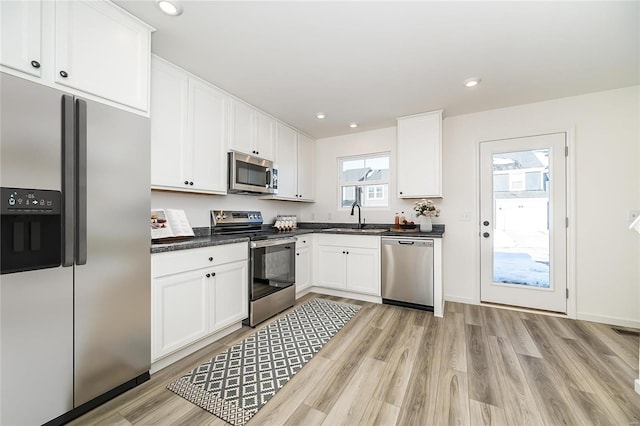 kitchen featuring a sink, white cabinets, appliances with stainless steel finishes, light wood finished floors, and dark countertops