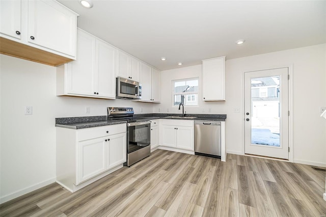 kitchen featuring stainless steel appliances, dark countertops, light wood-style flooring, white cabinets, and a sink