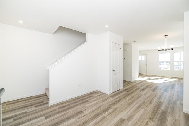 unfurnished living room with recessed lighting, an inviting chandelier, light wood-style floors, baseboards, and stairs