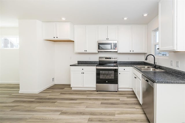 kitchen featuring light wood finished floors, white cabinets, dark countertops, appliances with stainless steel finishes, and a sink