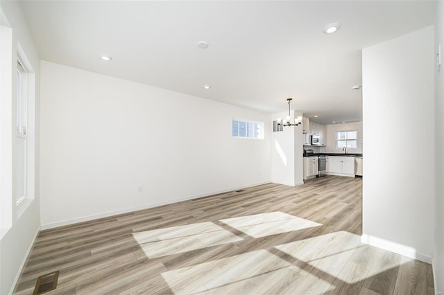 unfurnished living room featuring baseboards, visible vents, light wood-type flooring, a notable chandelier, and recessed lighting