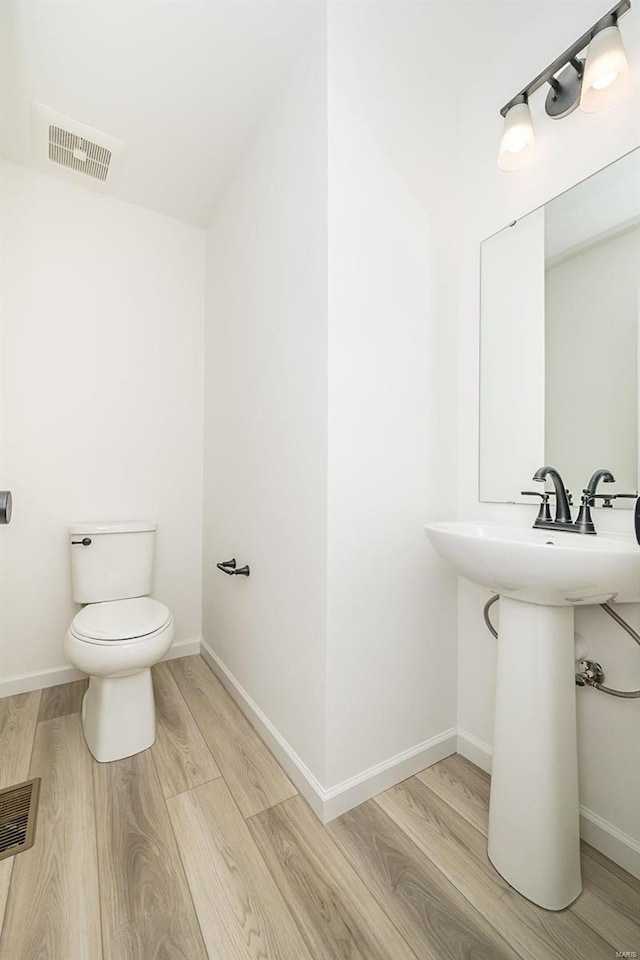 half bath featuring toilet, wood finished floors, visible vents, and baseboards