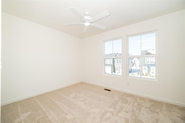 spare room with a ceiling fan, light colored carpet, visible vents, and baseboards