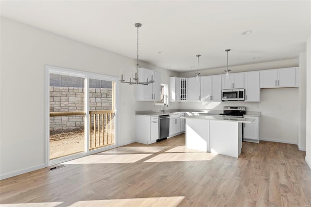 kitchen with a center island, sink, stainless steel appliances, decorative light fixtures, and white cabinets