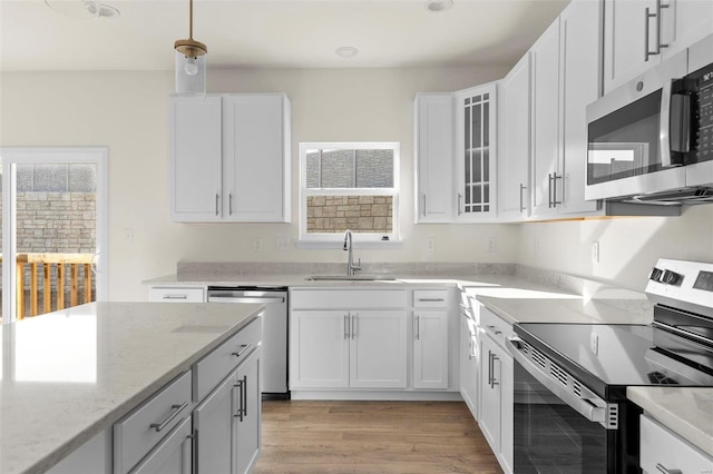 kitchen featuring light stone countertops, stainless steel appliances, sink, white cabinets, and hanging light fixtures