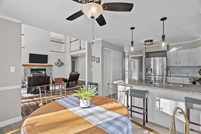 dining space with a fireplace, ceiling fan, crown molding, and sink