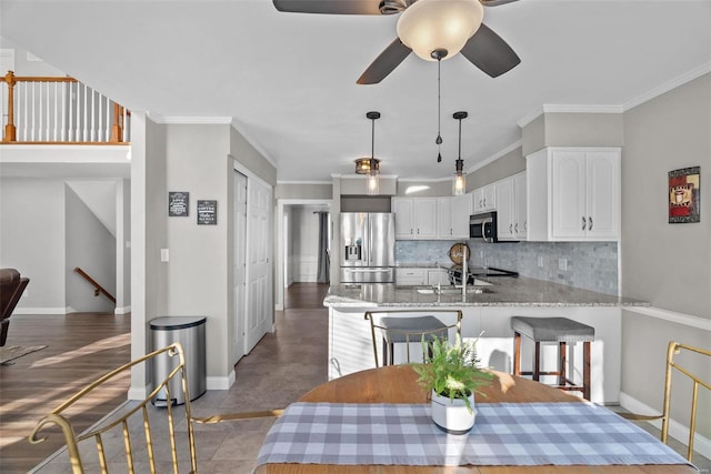 kitchen featuring kitchen peninsula, stainless steel appliances, tasteful backsplash, white cabinetry, and ornamental molding