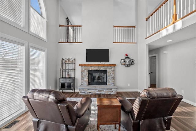 living room featuring a high ceiling, wood-type flooring, and a stone fireplace