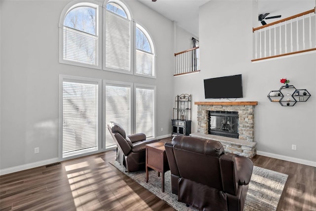 living room featuring a towering ceiling, ceiling fan, dark hardwood / wood-style flooring, and a stone fireplace