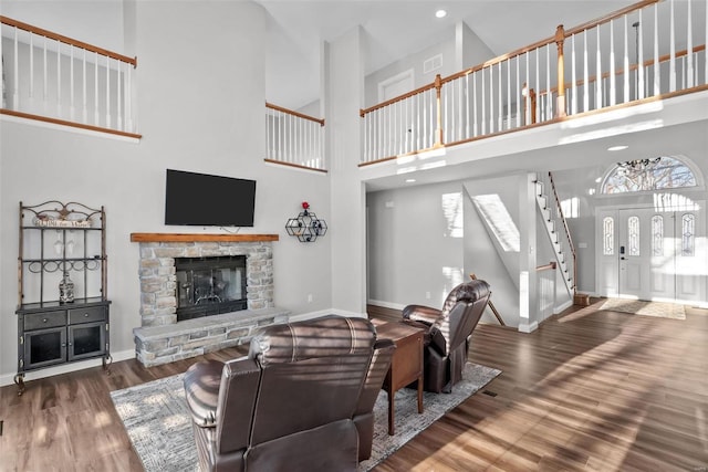 living room featuring a towering ceiling, wood-type flooring, and a stone fireplace