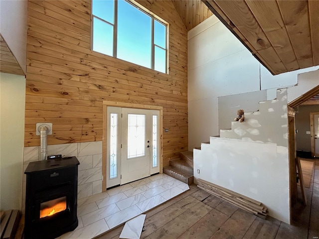 entryway with high vaulted ceiling, light wood-type flooring, a wood stove, and wooden walls