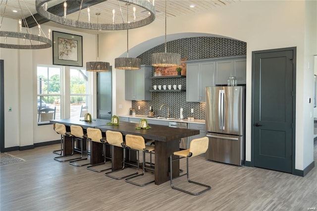 kitchen featuring gray cabinetry, stainless steel fridge, light wood-type flooring, and decorative light fixtures