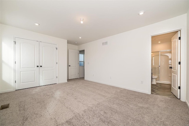 unfurnished bedroom featuring light colored carpet, ensuite bathroom, and a closet