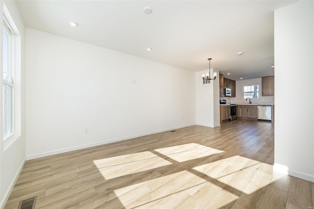 unfurnished living room with a notable chandelier, sink, and light hardwood / wood-style floors