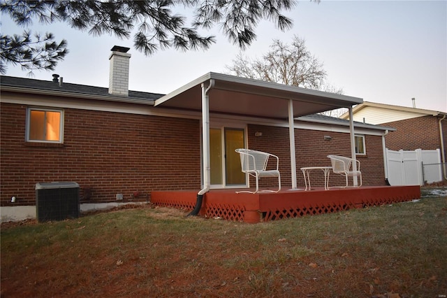 rear view of house with central AC unit, a lawn, and a deck