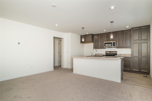 kitchen with appliances with stainless steel finishes, decorative light fixtures, sink, dark brown cabinetry, and a center island with sink