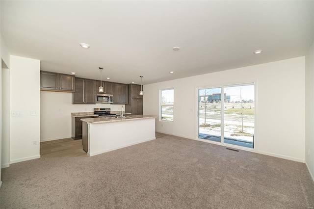 kitchen with sink, hanging light fixtures, stainless steel appliances, a center island with sink, and light carpet