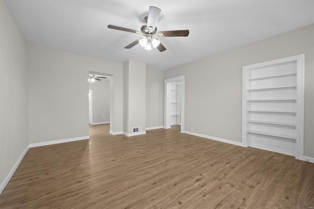 spare room with built in shelves, ceiling fan, and wood-type flooring