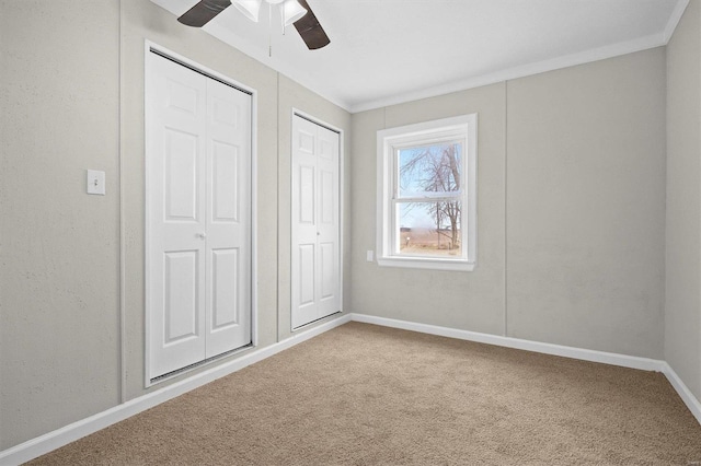 unfurnished bedroom with carpet flooring, ornamental molding, ceiling fan, and multiple closets