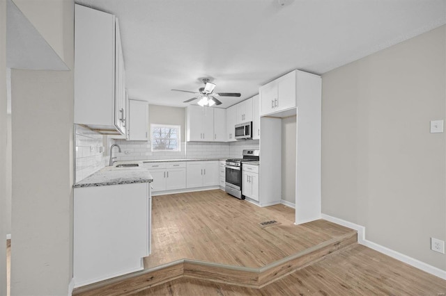 kitchen with light stone countertops, tasteful backsplash, light hardwood / wood-style flooring, white cabinets, and appliances with stainless steel finishes