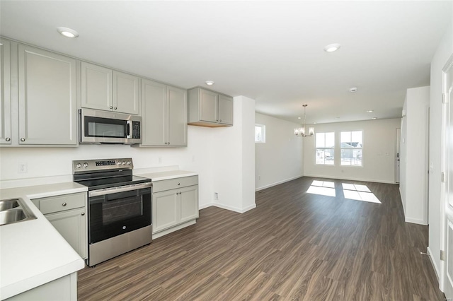 kitchen with gray cabinets, appliances with stainless steel finishes, hanging light fixtures, dark wood-type flooring, and an inviting chandelier