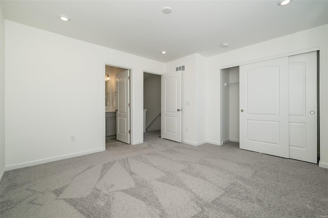 unfurnished bedroom with light colored carpet, ensuite bathroom, and a closet