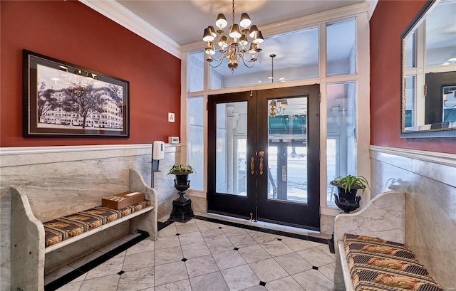 tiled entrance foyer with an inviting chandelier, ornamental molding, french doors, wainscoting, and tile walls