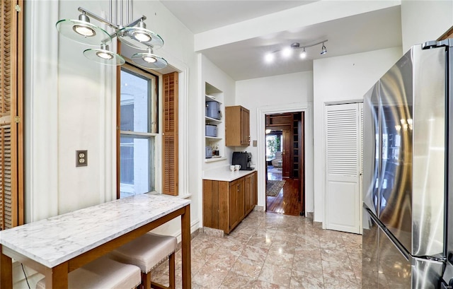 kitchen with brown cabinetry, open shelves, freestanding refrigerator, light countertops, and a notable chandelier